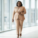 Comment choisir une tenue professionnelle flatteuse en grande taille Femme grande taille en tenue de bureau élégante, blazer structuré et pantalon droit, marchant dans un environnement professionnel lumineux.